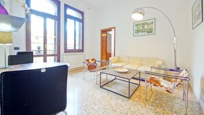 A living room with a sofa, coffee table, and a lamp. There is a window with blinds, a radiator, and a door. - DolceVita Apartments N. 331 (Venice)