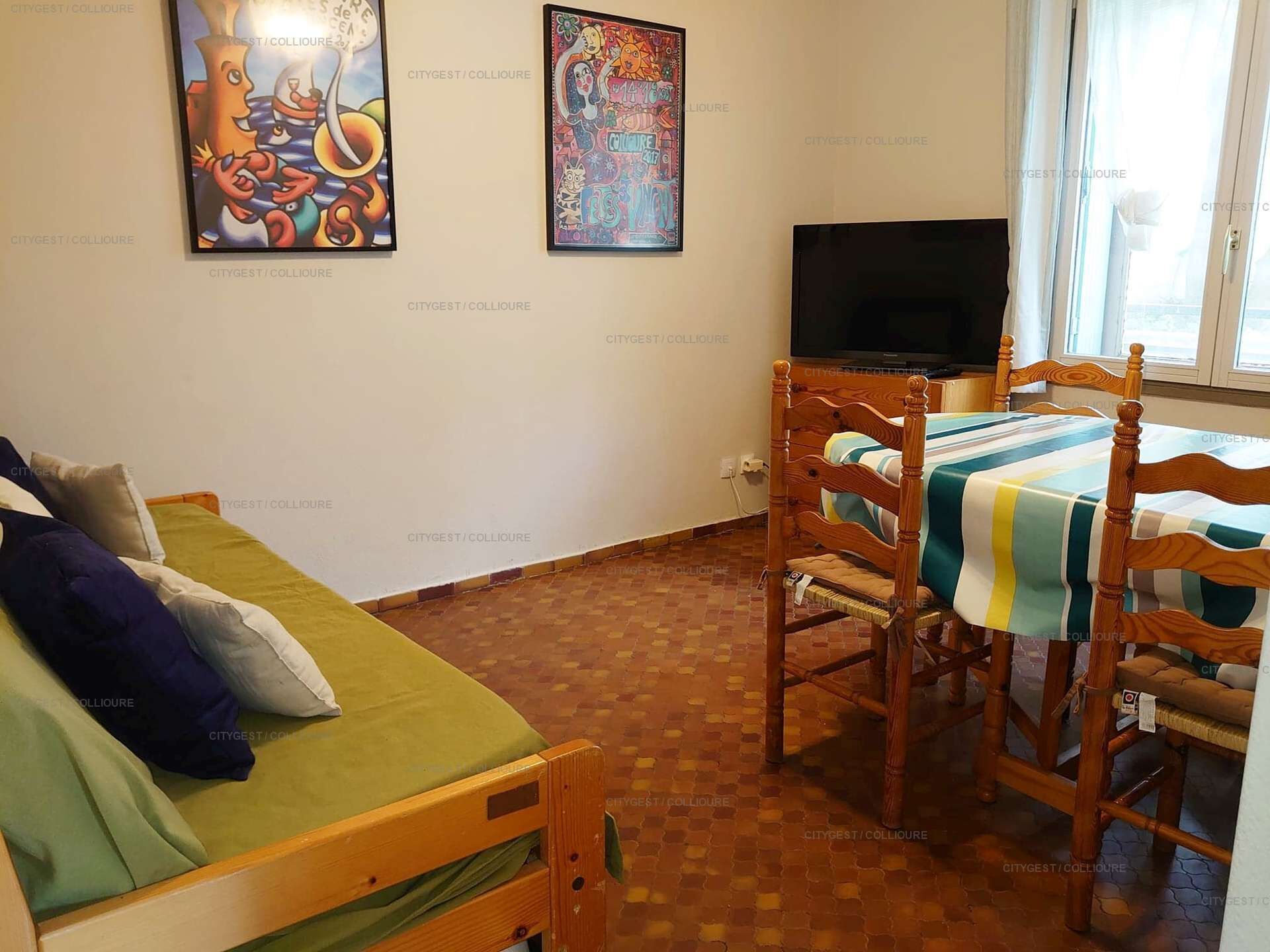 Een kamer met een bed, een tafel met stoelen, een televisie en twee kunstwerken aan de muur.