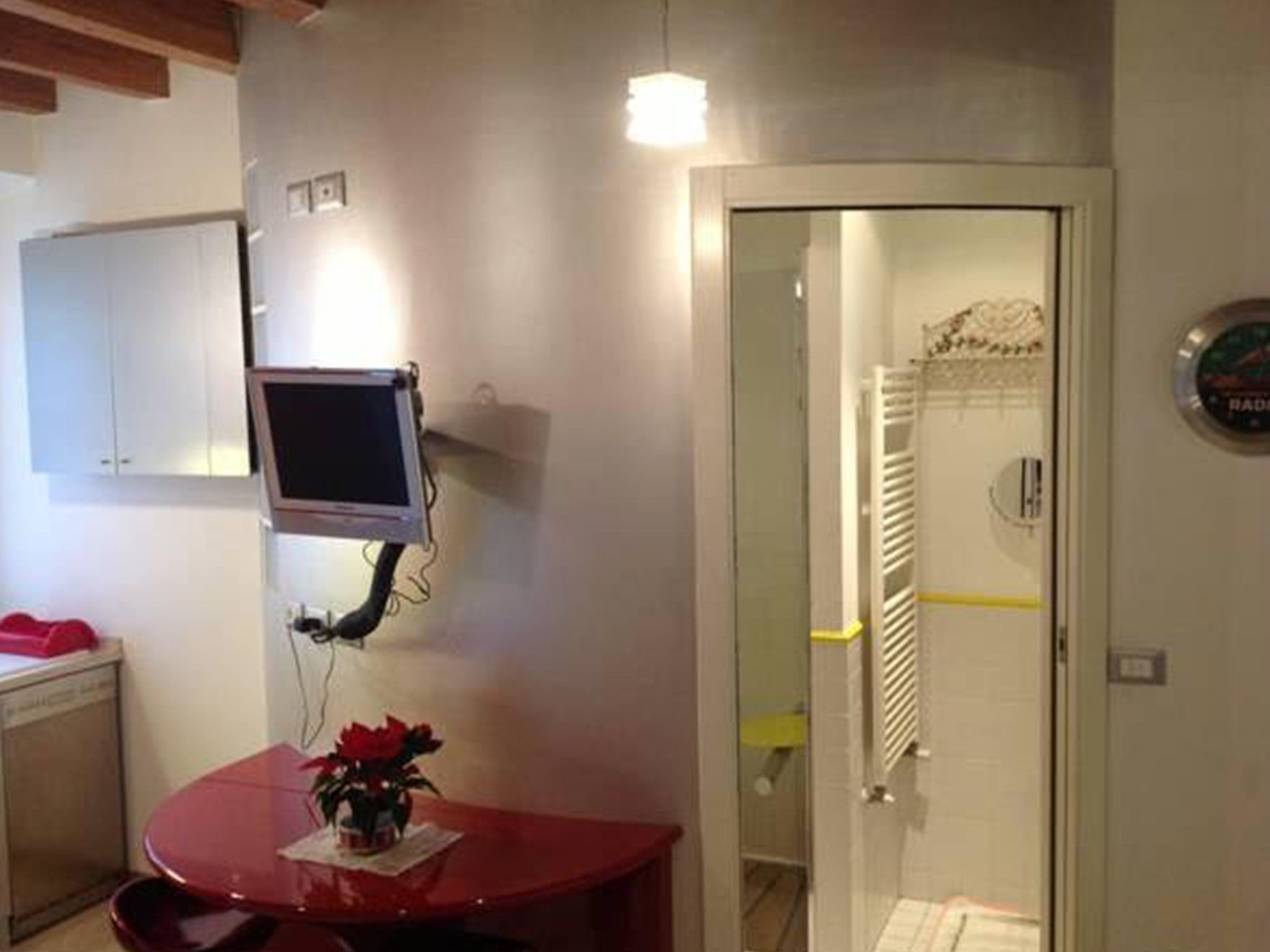 A compact room with a small table, a chair, a potted plant, a wall-mounted TV, and a door leading to a bathroom.