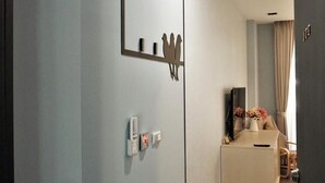 Habitación de hotel moderna con un espejo grande, un televisor de pantalla plana, una mesita con un florero y suelo de madera.