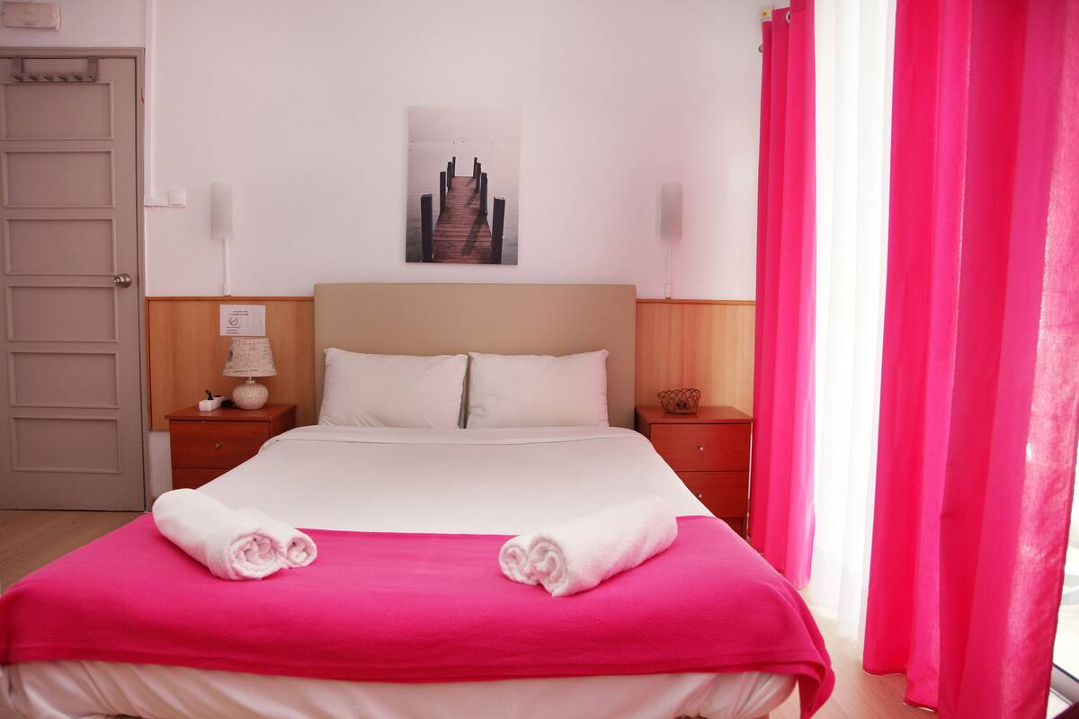 Une chambre d’hôtel avec un lit, deux tables de chevet, une horloge murale, un tableau encadré et une porte.