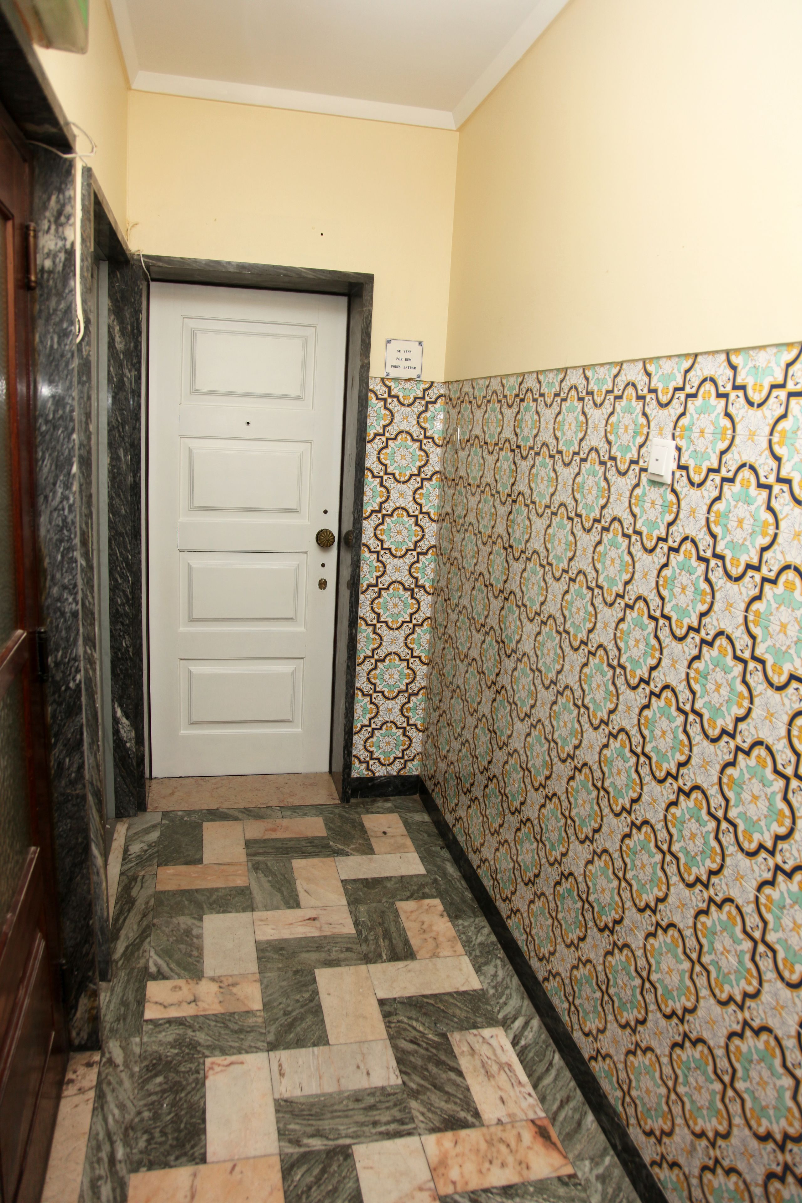 A hallway with a patterned wall, a white door, and a marble floor.