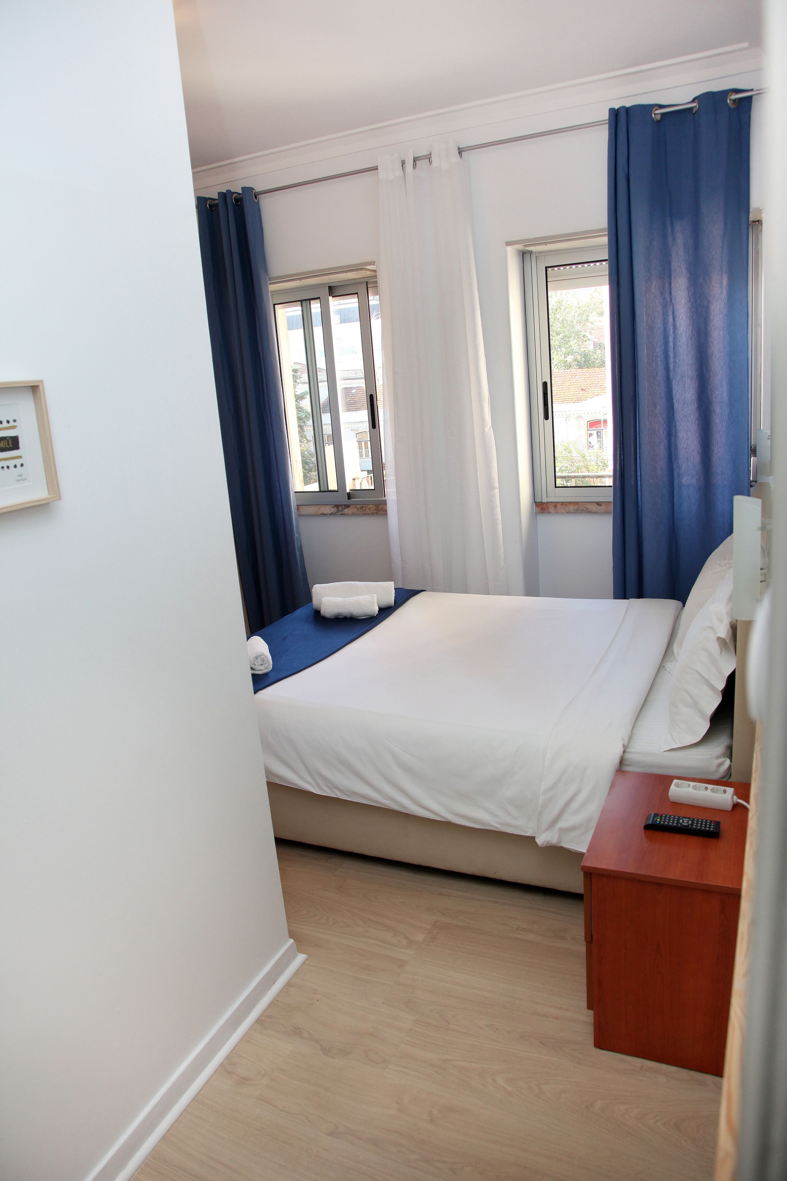 Una habitación de hotel con una cama, una mesita de noche con control remoto y una ventana con cortinas.