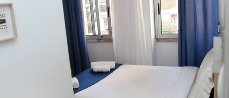 Una habitación de hotel con una cama, una mesita de noche con control remoto y una ventana con cortinas.