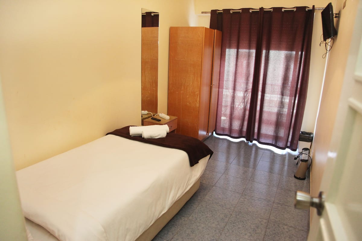 Une chambre d’hôtel avec un lit, une armoire en bois, un miroir et un rideau.