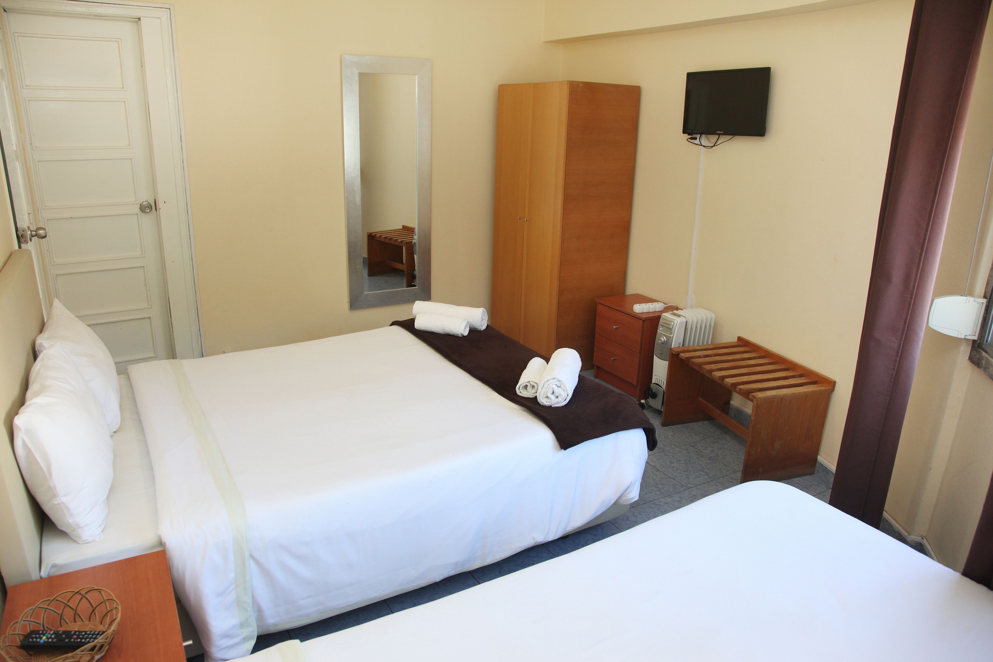 A hotel room with two beds, a wardrobe, a mirror, a television, and a small table with a remote control.