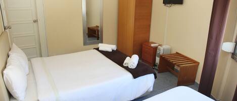 A hotel room with two beds, a wardrobe, a mirror, a television, and a small table with a remote control.