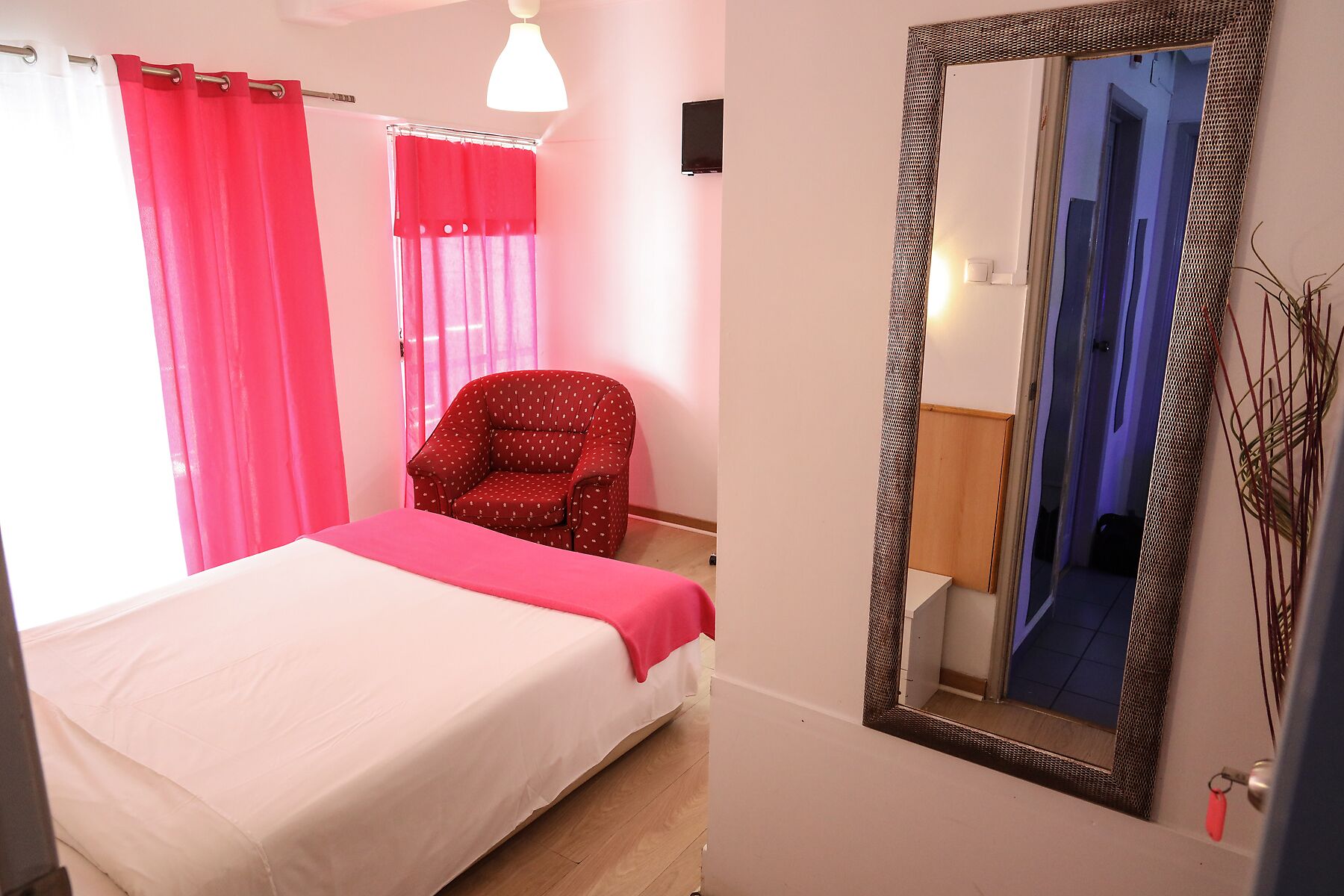 Un dormitorio con cama, una silla, un espejo y cortinas.