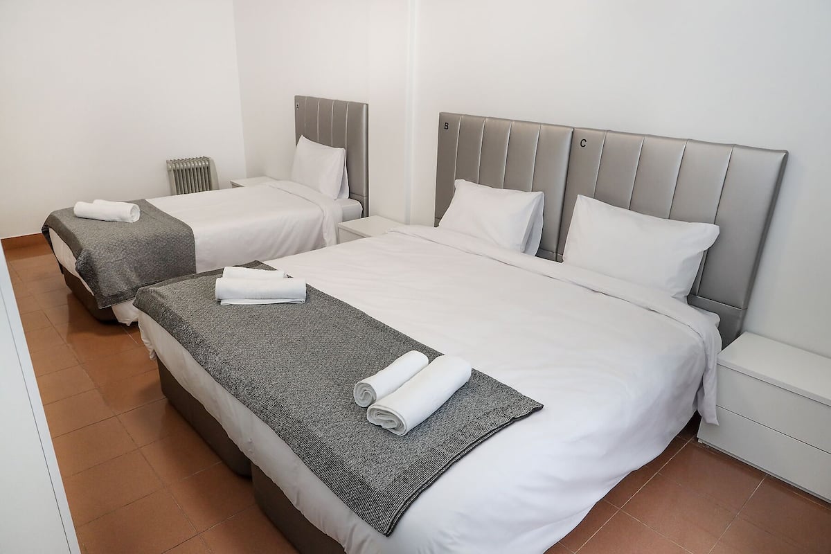 Une chambre d’hôtel avec deux lits simples, chacun doté d’une tête de lit grise et de linge de lit blanc.