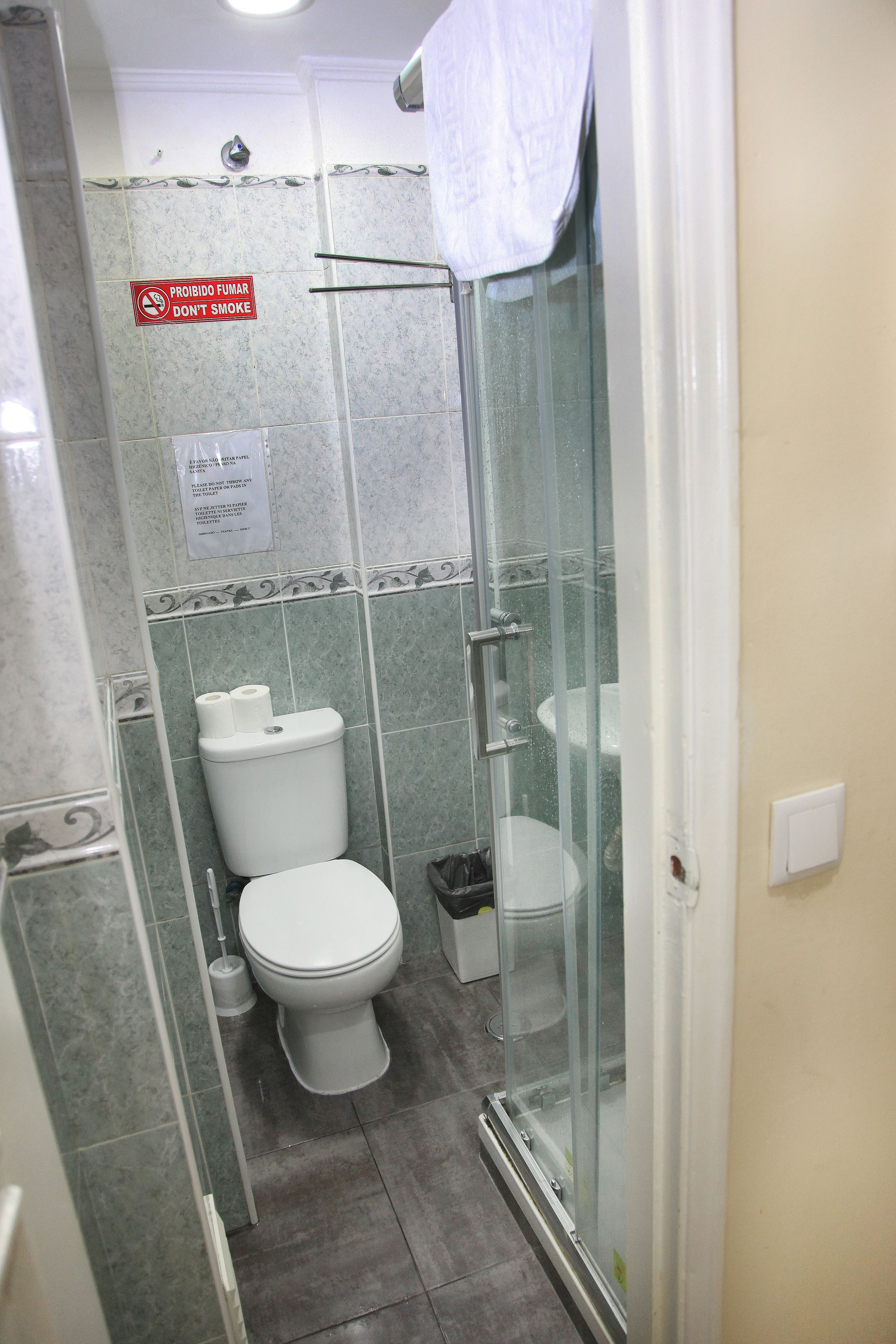 Een badkamer met een douchecabine van glas, een toilet en een bordje met de tekst 'Niet roken'.