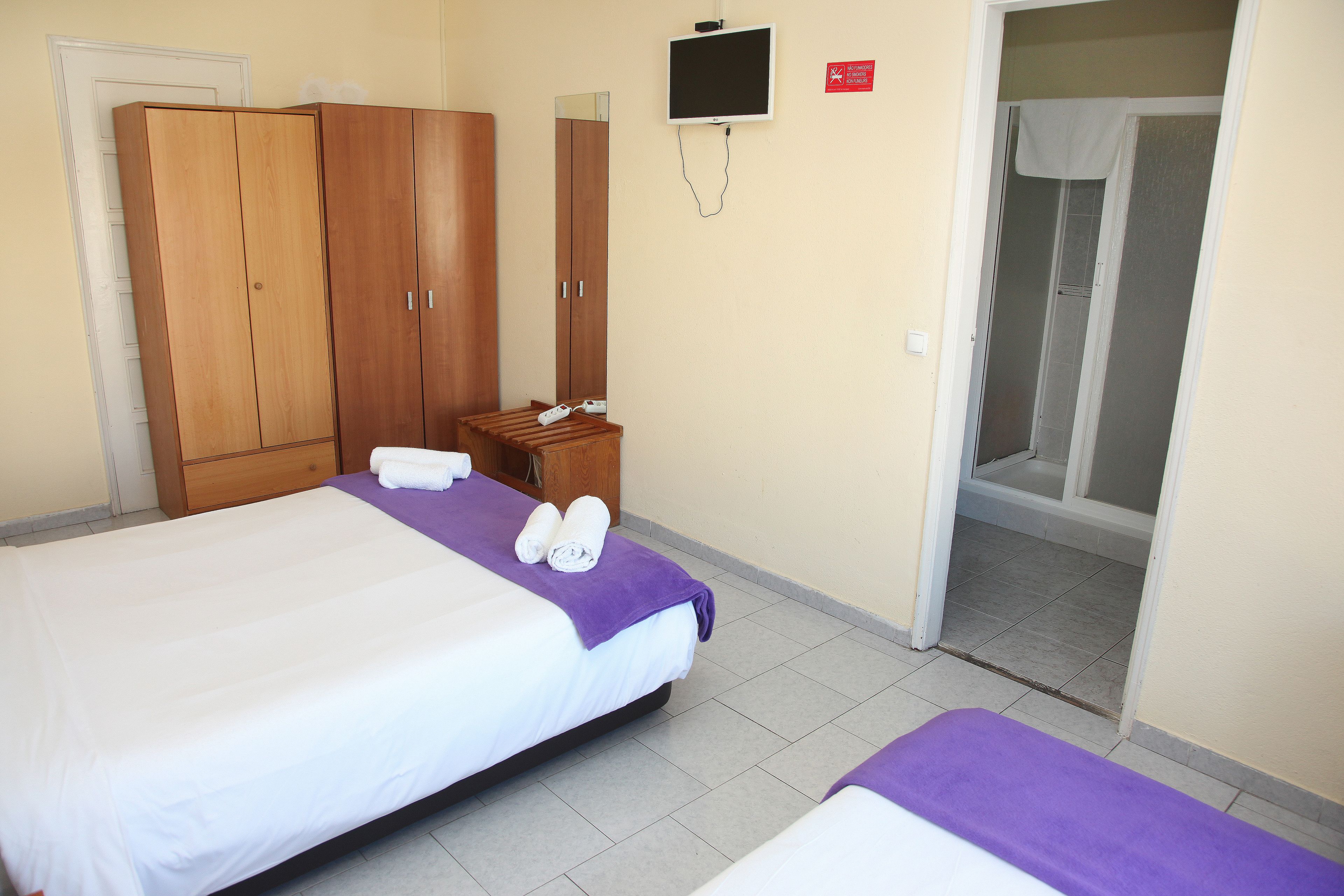 Une chambre d’hôtel avec deux lits, une armoire en bois, une télévision et un espace douche.