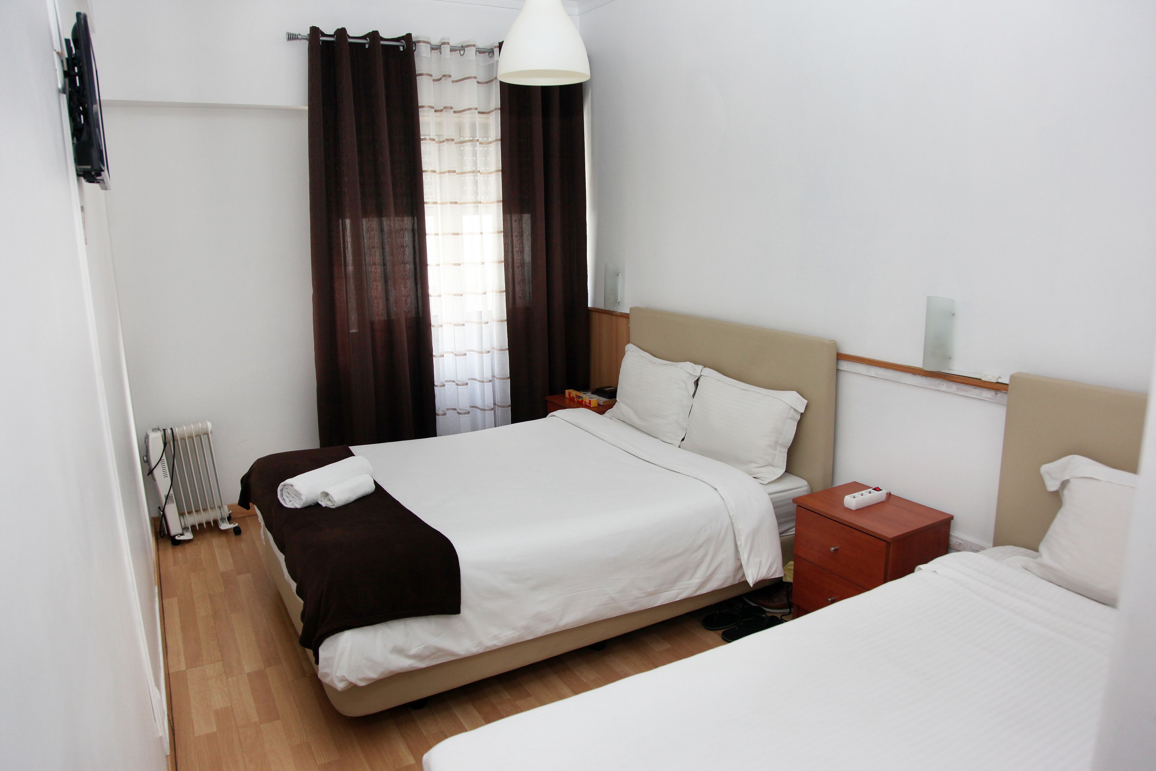 A hotel room with a bed, bedside table, nightstand, and a radiator.