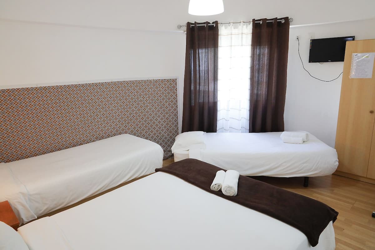 Une chambre d’hôtel avec deux lits simples, une armoire en bois, un téléviseur fixé au mur et une tête de lit à motifs.