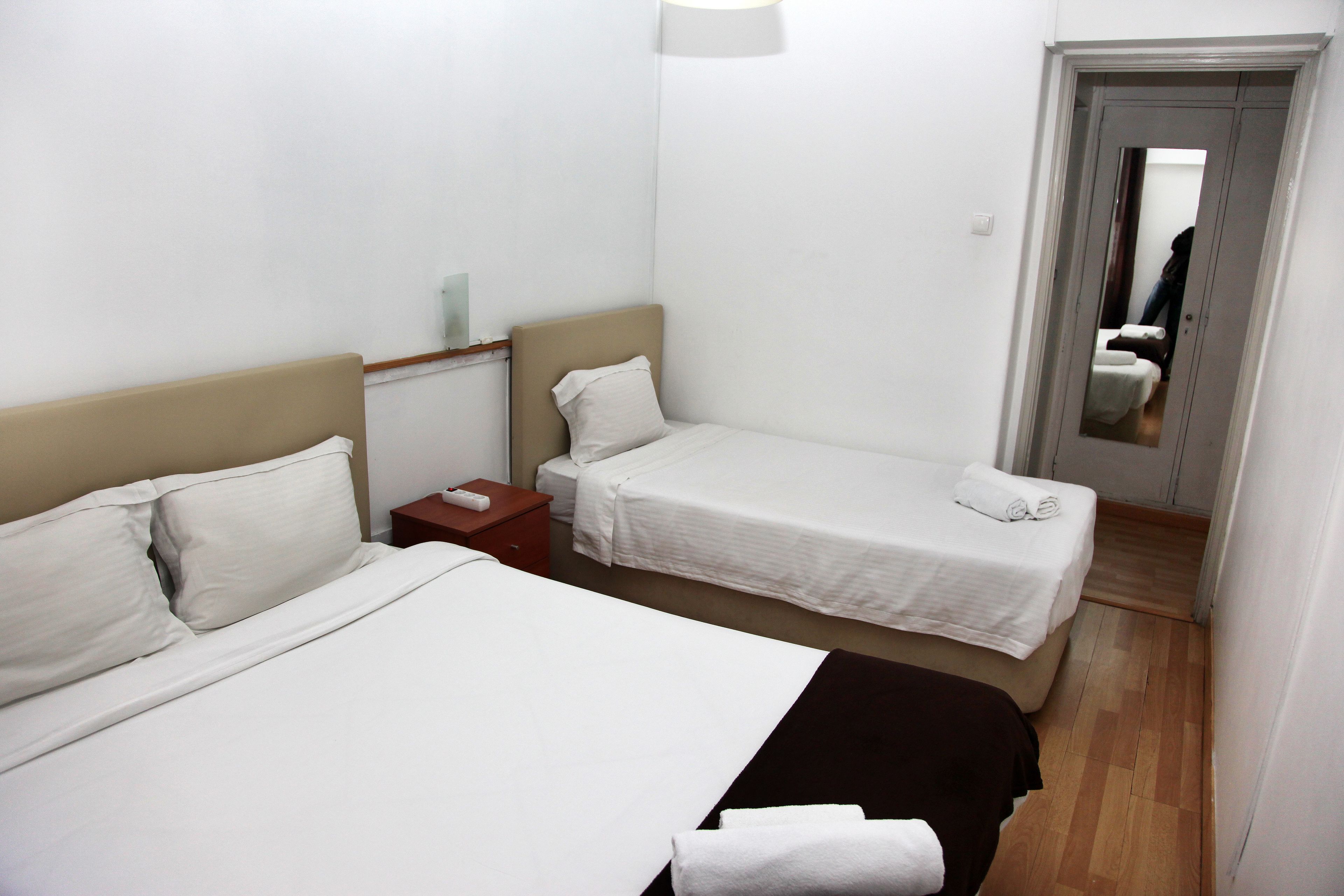 A hotel room with two single beds, a nightstand, a bedside table, and a mirror.
