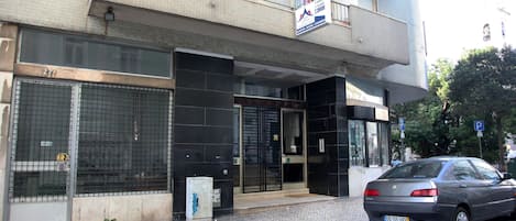 Un edificio con entrada negra, se ve el número 27 en la puerta, y un coche estacionado.