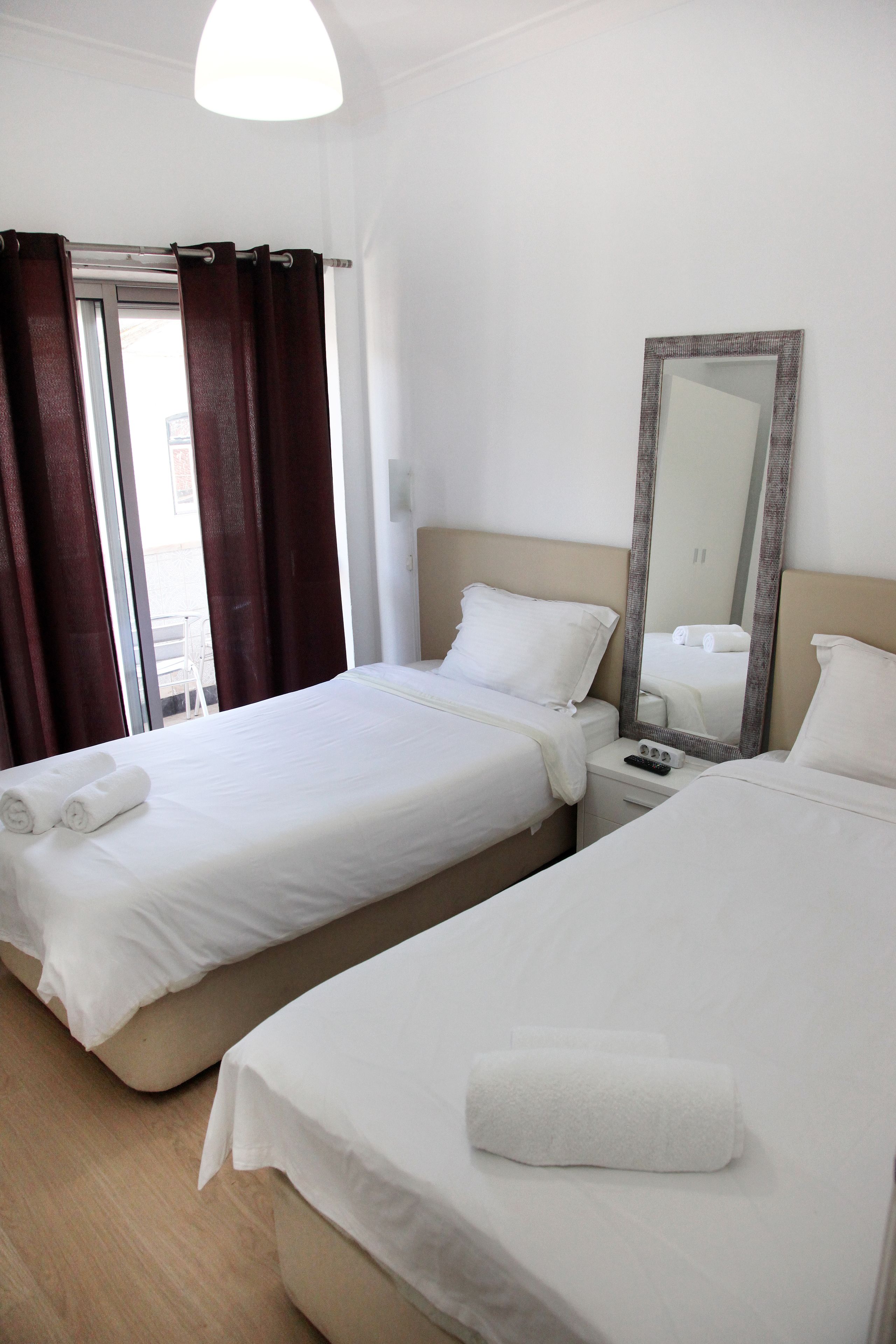 A hotel room with two beds, a large mirror, a bedside table, and a window with curtains.