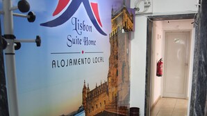 A Lisbon Suite Home reception area with a welcome mat, a wall mural of a historic building, and a fire extinguisher. - Lisbon Suite Home (Lisbon)