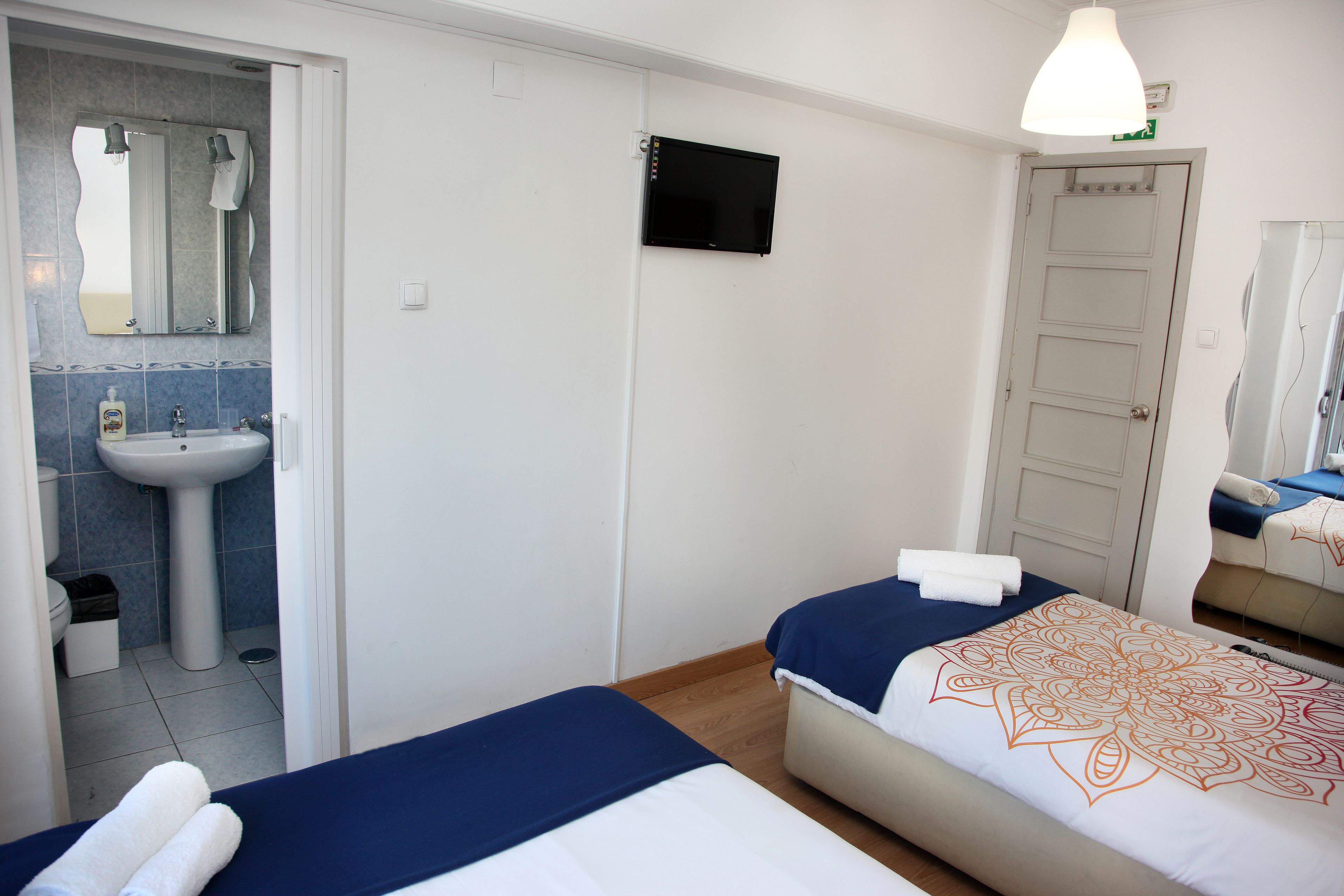 A hotel room with two beds, a sink, a mirror, and a television.