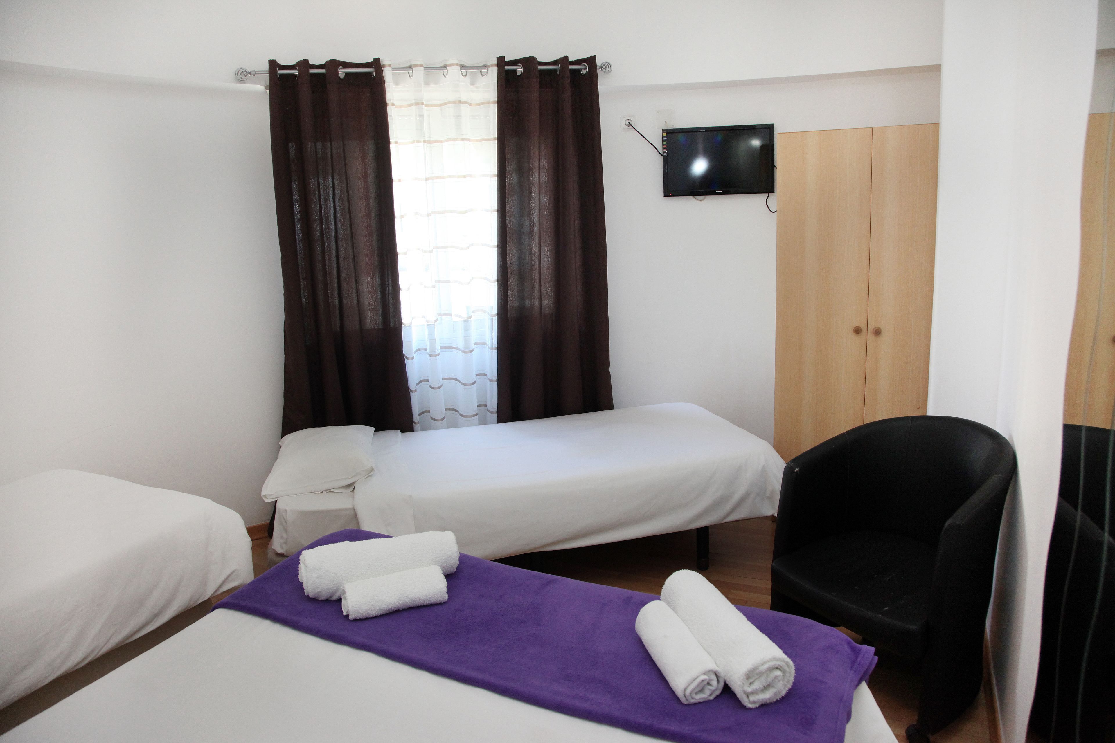 Een hotelkamer met twee eenpersoonsbedden, een stoel, een televisie en een garderobe.