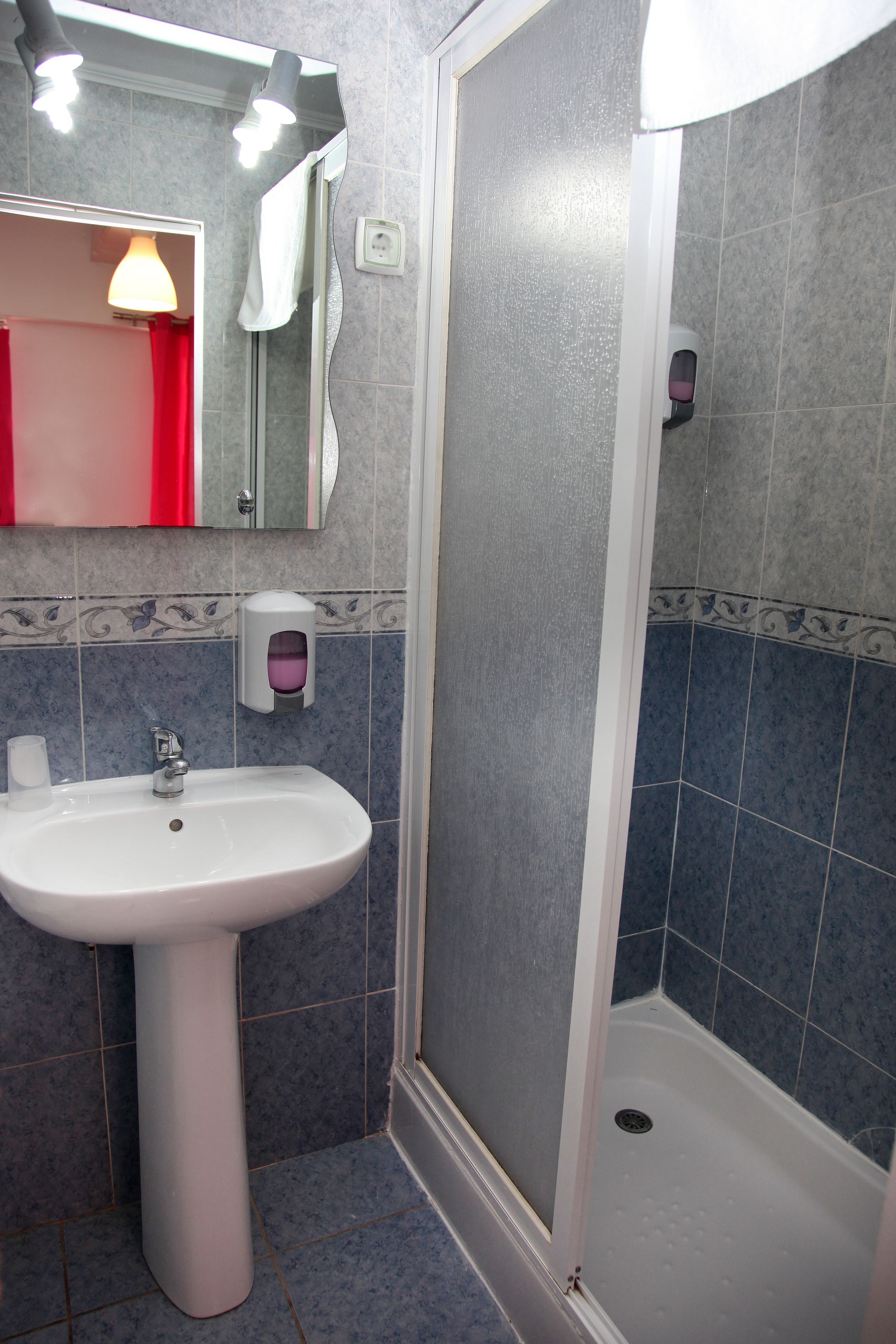 Un baño con lavamanos blanco, un espejo, una cortina roja y una zona de ducha.