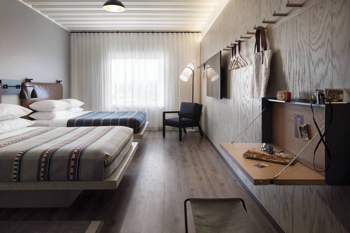 Ein modernes Hotelzimmer mit zwei Betten, einem Schreibtisch, einem Stuhl, einem Fernseher und einem Regal mit persönlichen Gegenständen.
