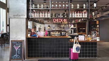Una zona de bar con un cartel que dice 'CHECK-IN', un cartel de 'BIENVENIDOS' y una pizarra con una promoción de bebidas.