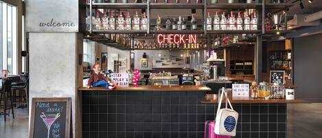 Eine Bar mit einem 'CHECK-IN'-Schild, einem 'WELCOME'-Schild und einer Tafel mit Getränkeangeboten.