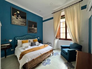 A bedroom with a large bed, a blue armchair, and two wall-mounted pictures. - Sibilla Napoli (Naples)