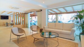 Un hall d’hôtel moderne avec un canapé, deux fauteuils en osier, une table basse en verre et un téléviseur fixé au mur.