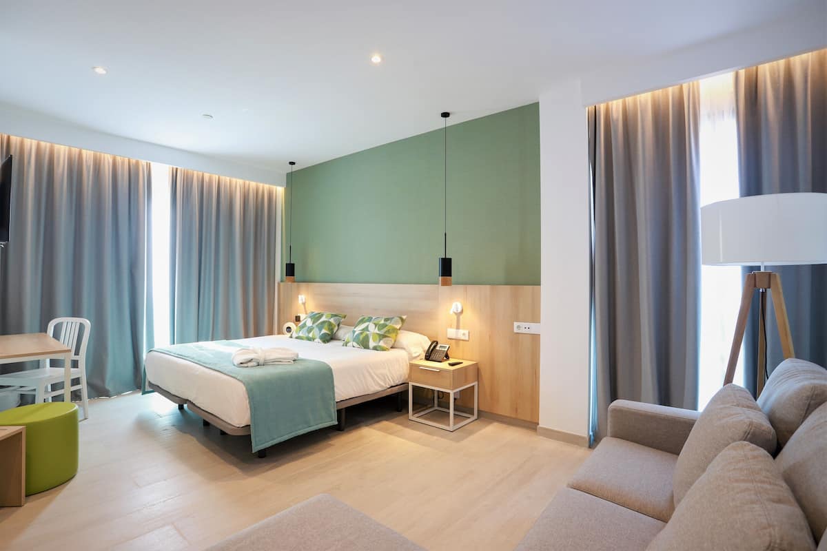 Una habitación de hotel moderna con cama, mesita de noche, lámpara y zona de estar.