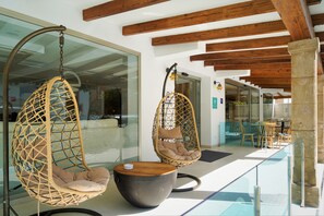 Een modern interieur met twee hangstoelen, een ronde tafel en een glazen balustrade met uitzicht op een eetgedeelte.