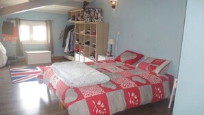 Un dormitorio con cama, un armario, estante con varios objetos y ventana con cortinas.