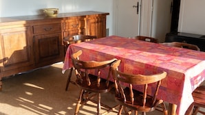 A dining area with a table covered by a floral tablecloth, wooden chairs, a wooden cabinet, and a door in the background. - Homerez - Chalet in Métabief (Métabief)