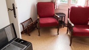 A room with a red upholstered chair, a wooden chair, a small round table, and a black metal bench. - Homerez - Chalet in Métabief (Métabief)