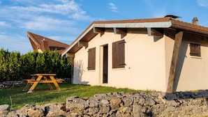 A single-story house with a sloped roof, wooden shutters, and a stone wall in the foreground. - Homerez - Chalet in Métabief (Métabief)