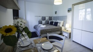 Un dormitorio moderno con cama, mesitas de noche, una mesa de comedor preparada para dos personas y un florero con flores.