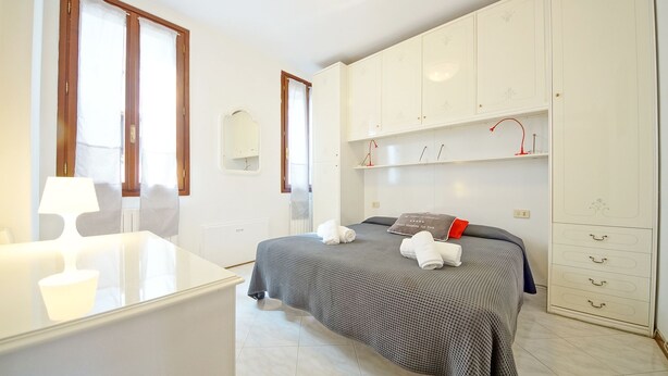 A bedroom with a bed, a desk, a chair, a wardrobe, and a window with curtains.