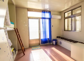 A room with a sliding door, a window with blinds, a radiator, a small table, a chair, and a wall-mounted air conditioner.