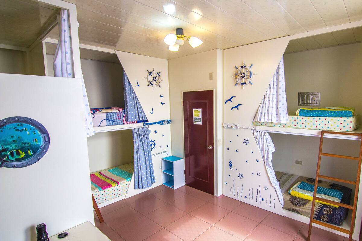A children's room with bunk beds, nautical-themed decorations, and a small window.
