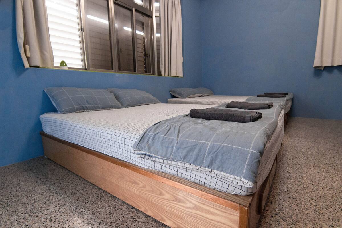 A bedroom with a large bed, two smaller beds, and a window with blinds.