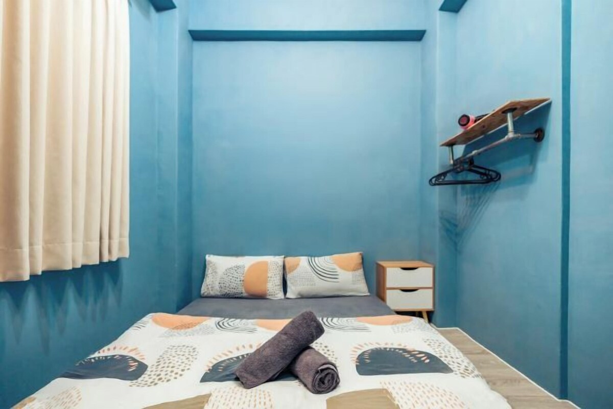 A bedroom with a bed, pillows, a bedside table, and a wall-mounted shelf.