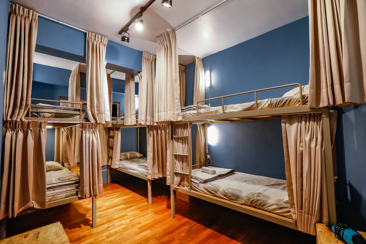 A dormitory room with bunk beds, curtains, and a wooden floor.