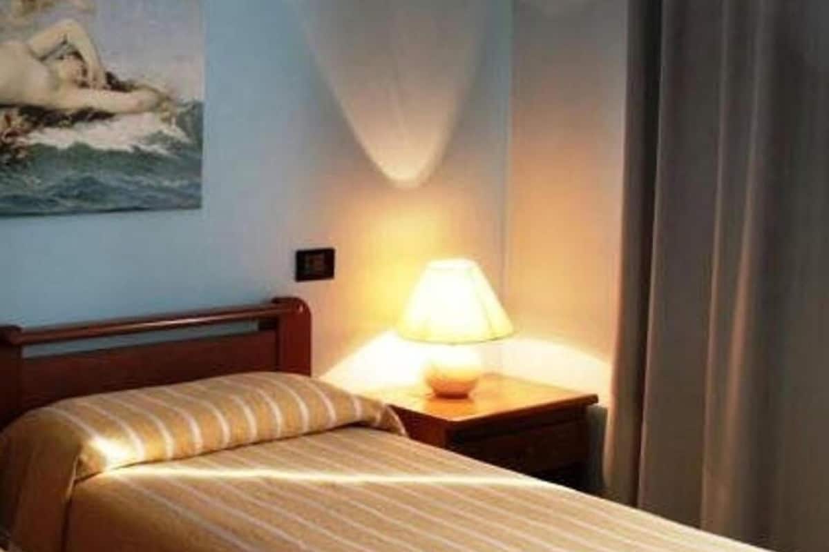 A hotel room with a bed, a nightstand with a lamp, and a painting on the wall.