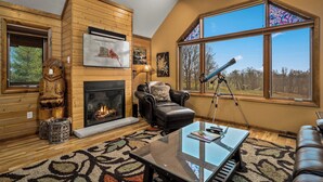 Una sala de estar acogedora con chimenea, sofá de cuero y un amplio ventanal con un telescopio.