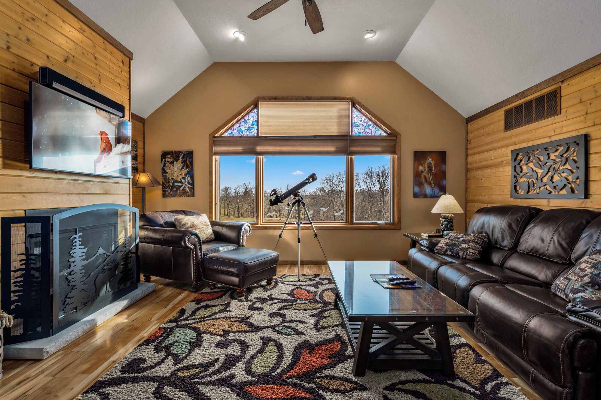 A spacious living room with a large window, a fireplace, a leather sofa, and a telescope.