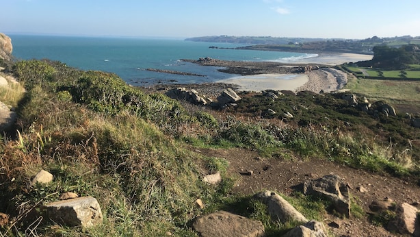 Ett kustlandskap med ett bergigt område, en sandstrand och utsikt över havet.