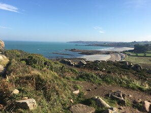 Eine Küstenlandschaft mit felsigem Gelände, einem Sandstrand und Blick aufs Meer.