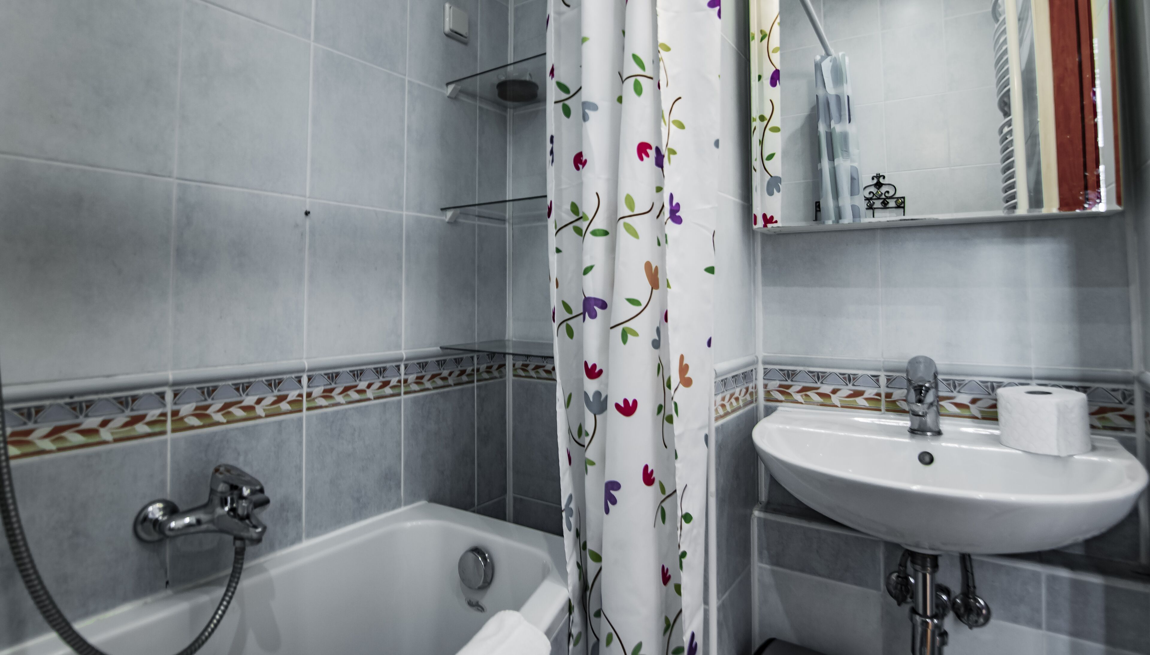 A bathroom with a bathtub, a sink, and a shower curtain with floral patterns.