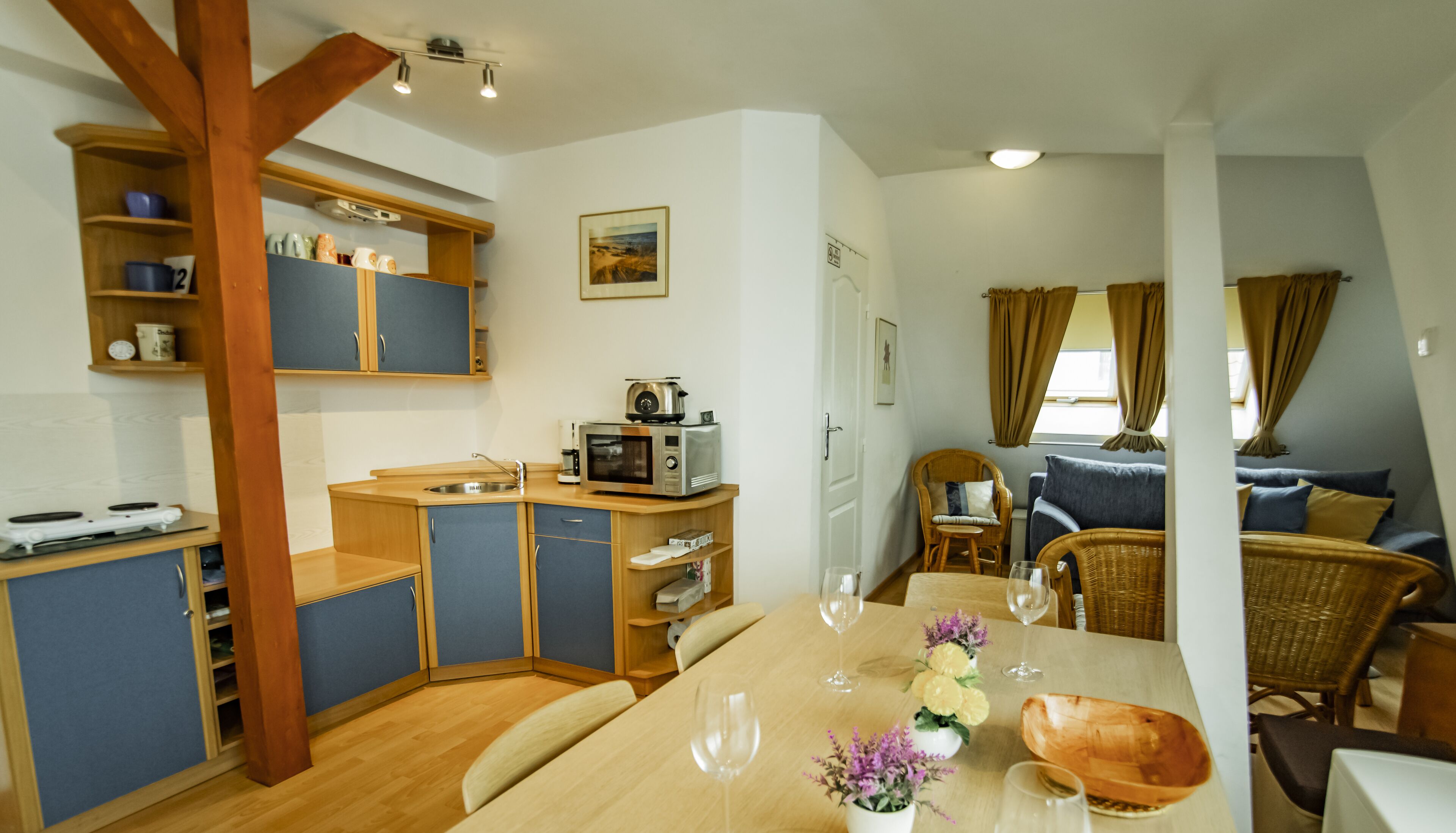 A compact kitchen with modern appliances, a dining area with a wooden table and chairs, and a cozy seating area with a sofa and wicker chairs.