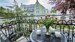 Een balkon met een metalen hekwerk, een ronde tafel met een bloemenvaas, en uitzicht op een groen gebouw met meerdere ramen.